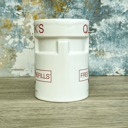 This white ceramic mug is a replica of Quark's Bar from Star Trek: Deep Space Nine, featuring "Quark's" and "Free Refills" printed on its surface.