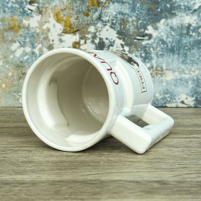 A white ceramic mug labeled "Quarks Bar" and "Free Refills" is tilted to show its empty interior against a textured background.