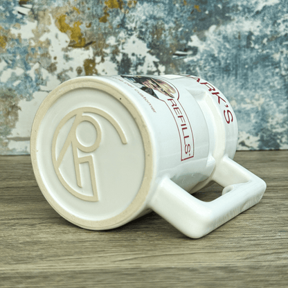 A white ceramic mug resembling a Quarks Bar replica features red lettering that reads "REFILLS" and a circular logo on its side.