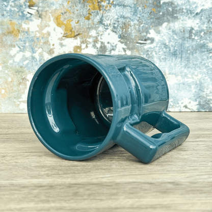 An empty green Ops Raktajino mug from Deep Space Nine sits on a wooden surface against a textured wall.