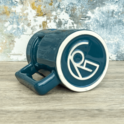 A teal Ops Raktajino mug from DS9 features a circular design with stylized "RG" lettering on the rim.