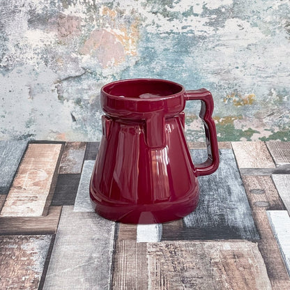 A red Raktajino replica mug resembling a Big Red Synth Ale stein from Quark's Bar on DS9 is displayed against a textured background.