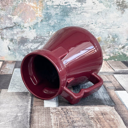 A deep red Raktajino replica mug resembling a Big Red Synth Ale vessel from Quark’s Bar in DS9 sits on a patterned surface.