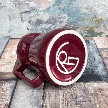 A red Raktajino Replica Mug from Quark's Bar on DS9 displays a white stylized logo inside a circle on its rim.