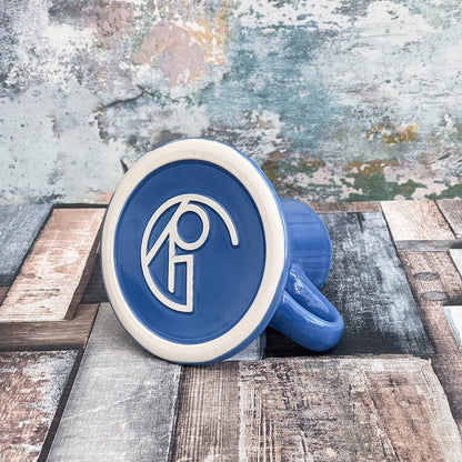 A blue Replimat mug from DS9 features a white logo design on its surface.