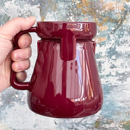 A hand holds a glossy red Raktajino Replica Mug resembling a Big Red Synth Ale container from Quark’s Bar in DS9.