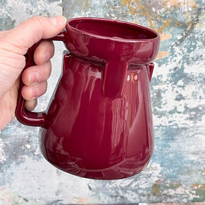 A hand holds a deep red Raktajino replica mug inspired by Big Red Synth Ale from Quark's Bar in DS9.
