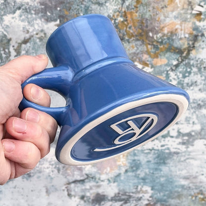 A hand holds a blue Little Blue Raktajino Replica Mug from DS9 featuring a Klingon symbol on its base.