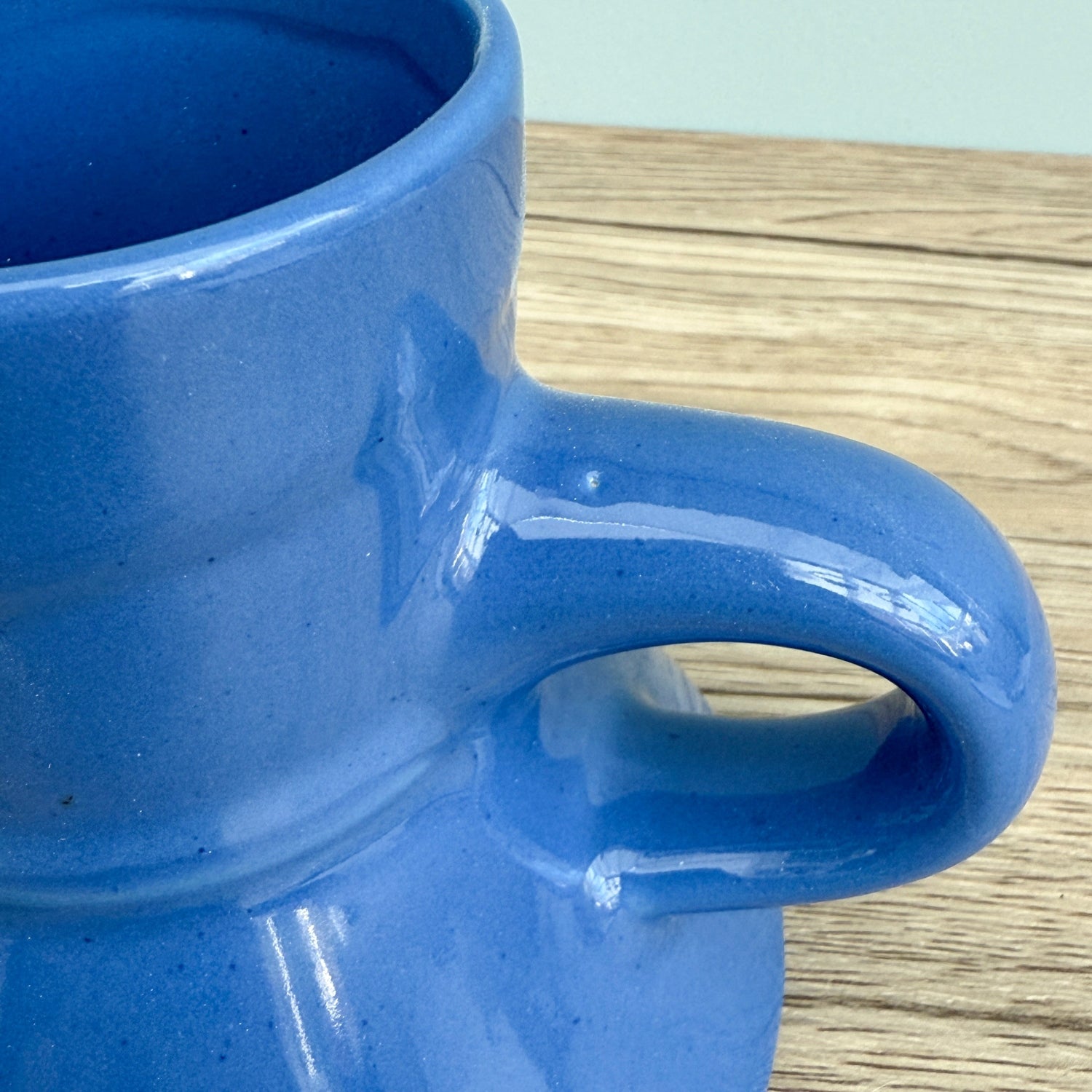 A blue handmade "Rejected Raktajino Mug" by Quirkify, featuring a wide flared base and handle, sits on a wooden surface. A white paper labeled "1" is in front, with a light blue background. Give one a good home today!.