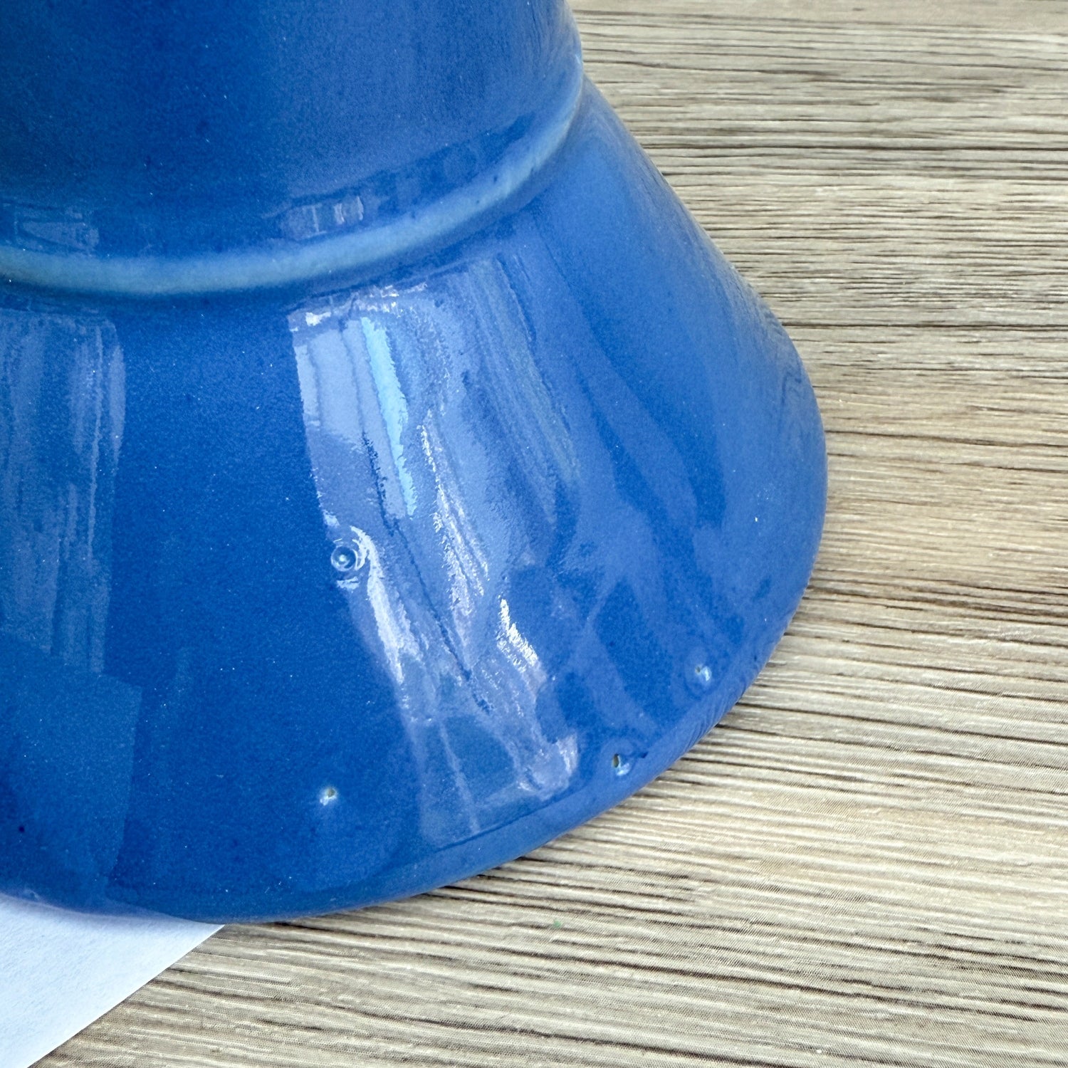 A blue handmade "Rejected Raktajino Mug" by Quirkify, featuring a wide flared base and handle, sits on a wooden surface. A white paper labeled "1" is in front, with a light blue background. Give one a good home today!.