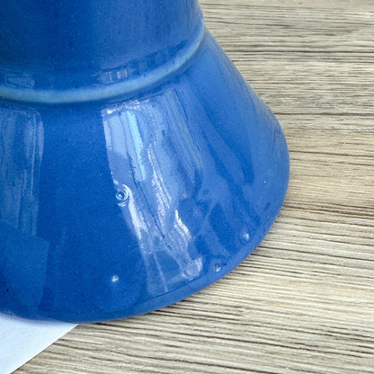 A blue handmade "Rejected Raktajino Mug" by Quirkify, featuring a wide flared base and handle, sits on a wooden surface. A white paper labeled "1" is in front, with a light blue background. Give one a good home today!.