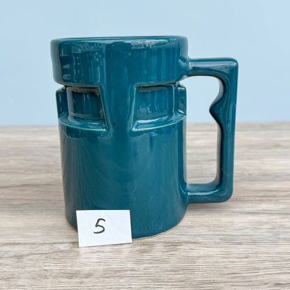 A handmade "Rejected Raktajino Mug" by Quirkify, sitting on a wooden surface. Give one a good home today!.