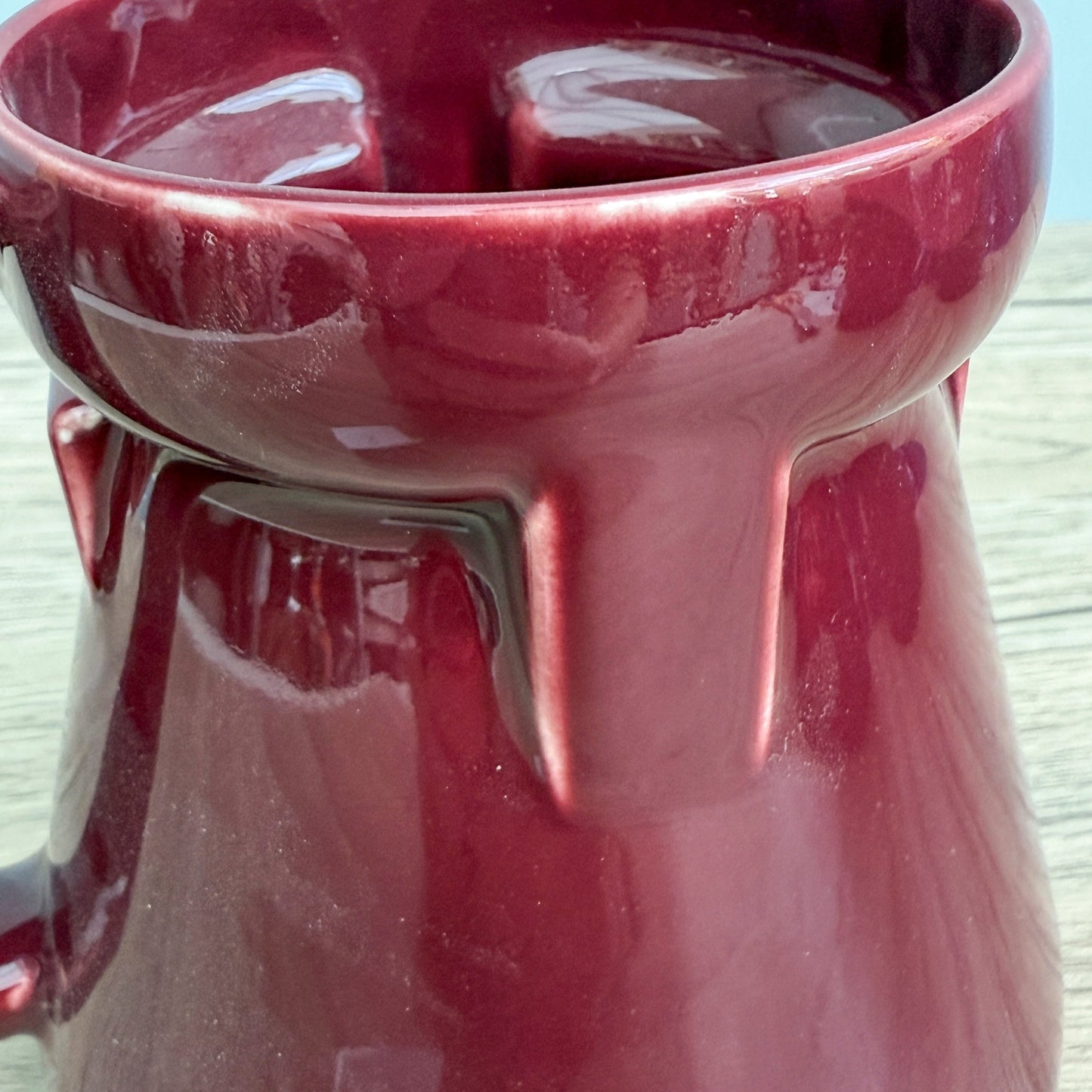 A red handmade "Rejected Raktajino Mug" by Quirkify, featuring a wide flared base and handle, sits on a wooden surface. Give one a good home today!.
