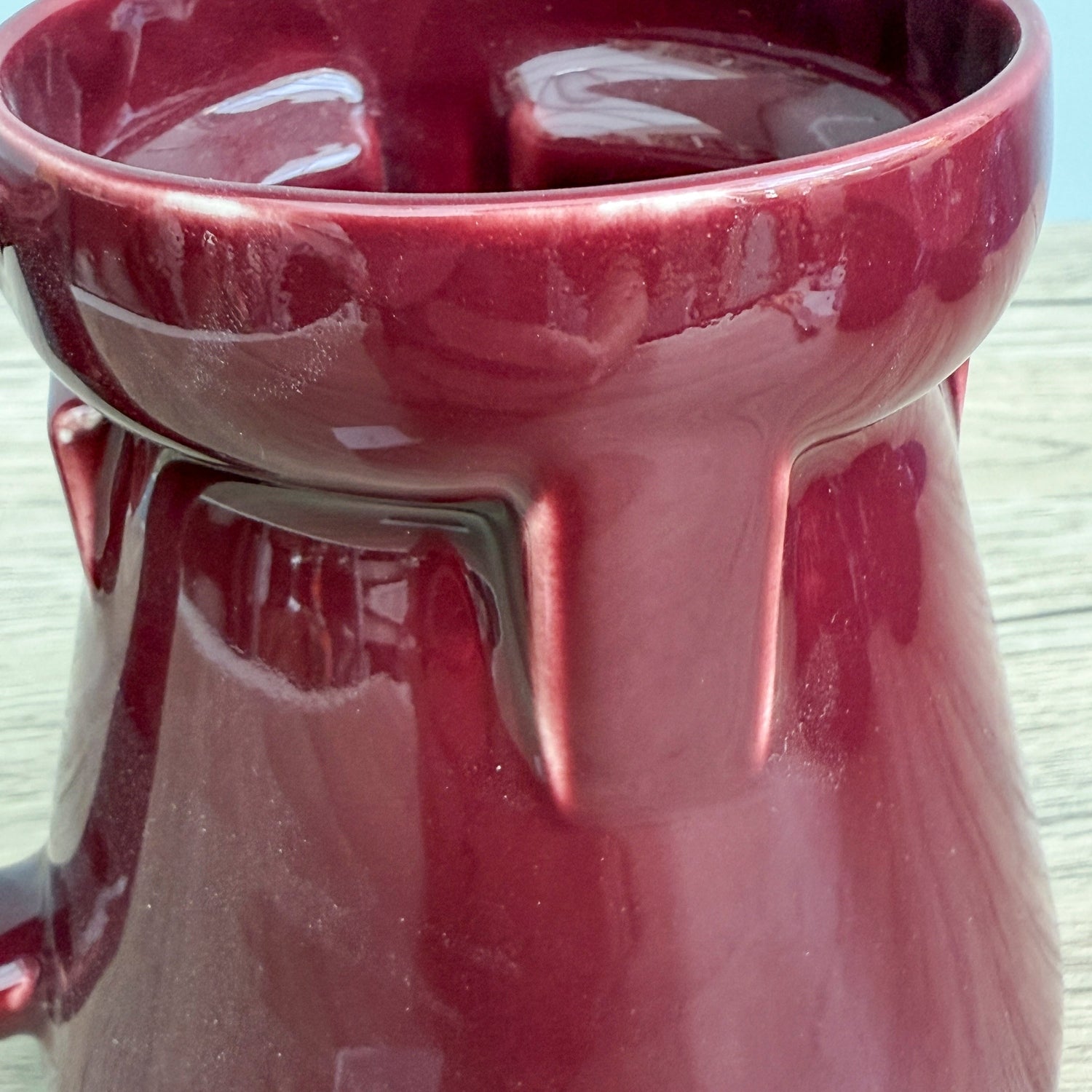A red handmade "Rejected Raktajino Mug" by Quirkify, featuring a wide flared base and handle, sits on a wooden surface. Give one a good home today!.