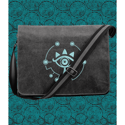 A black Zelda Sheikah messenger bag features glow-in-the-dark embroidery of a stylized eye symbol on the front flap and an adjustable shoulder strap.