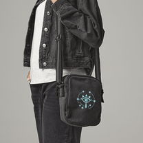A black Zelda Sheikah Tablet Bag is slung across a person's body and features glow-in-the-dark embroidery of an eye symbol.