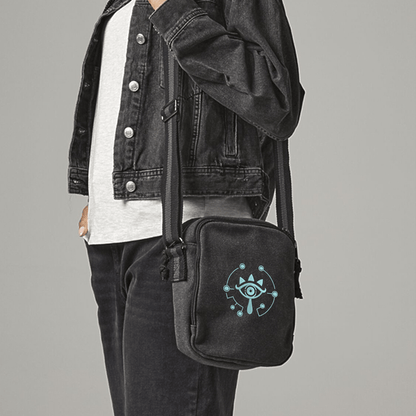 A black Zelda Sheikah Tablet Bag is slung across a person's body and features glow-in-the-dark embroidery of an eye symbol.