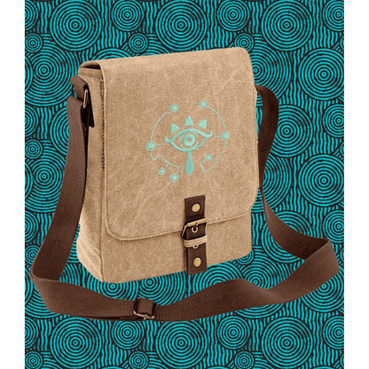 A tan Zelda Sheikah Tablet Bag features glow-in-the-dark embroidery of a stylized eye symbol on the front and a brown adjustable strap.