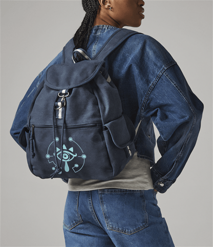 A person wears a dark blue Zelda Sheikah backpack featuring glow-in-the-dark embroidery of a stylized eye symbol.