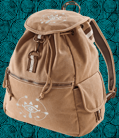 A brown Zelda Sheikah backpack features glow-in-the-dark embroidery of a stylized eye symbol on the front pocket and flap.