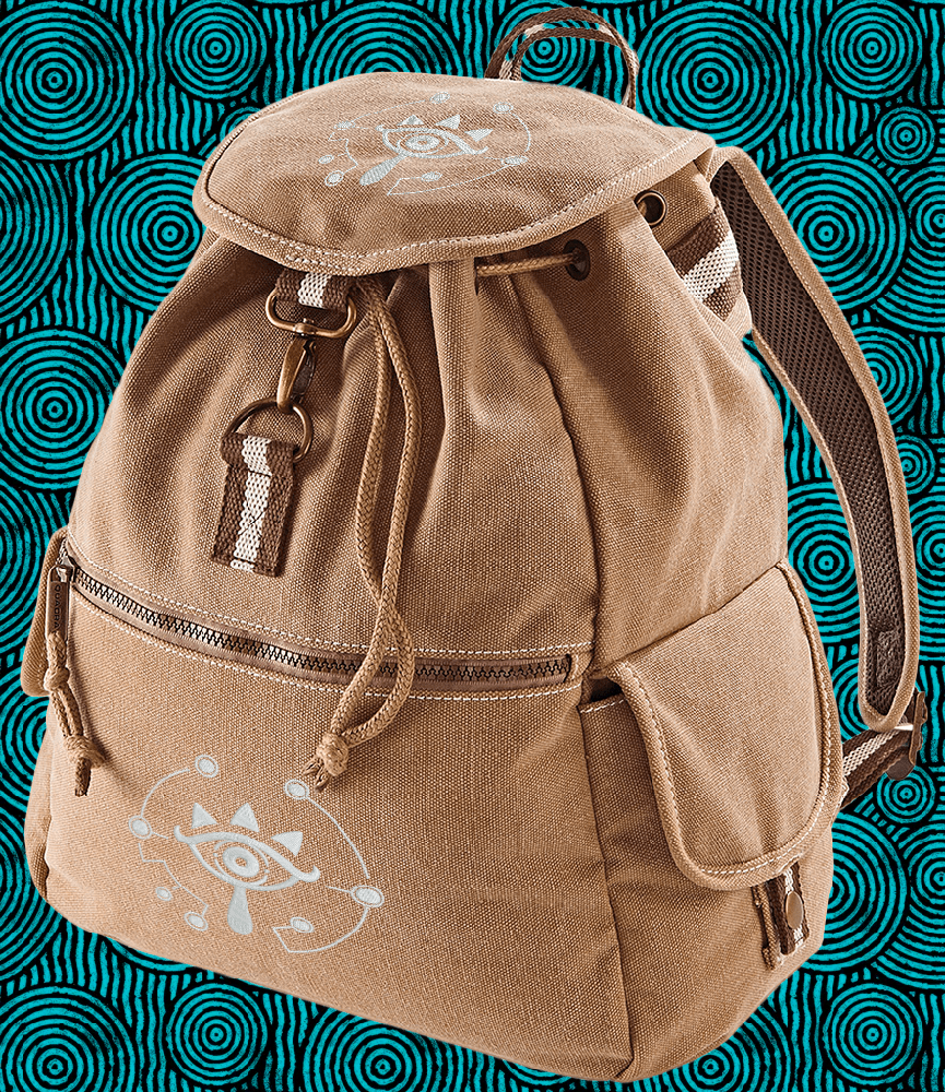 A brown Zelda Sheikah backpack features glow-in-the-dark embroidery of a stylized eye symbol on the front pocket and flap.