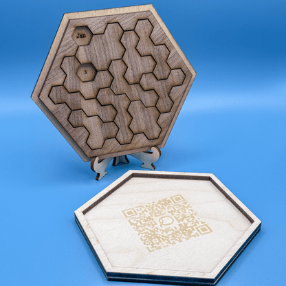 A wooden hexagonal perpetual calendar puzzle features interlocking hexominoes pieces arranged to display "Jan" and the number "1", alongside a QR code on a separate base piece.