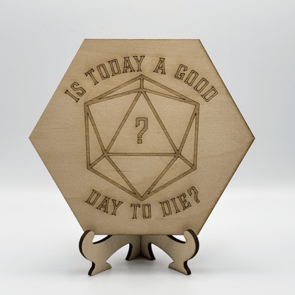 A wooden hexagonal puzzle calendar displays the phrase "Is today a good day to die?" surrounding an engraved D20 die with a question mark in its center, and is supported by a matching wooden stand.