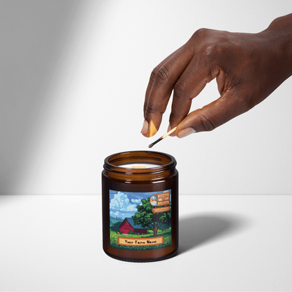 A hand holds a wooden skewer over a Stardew Valley scented candle featuring an illustration of a farm and personalized text reading "Your Farm Name.