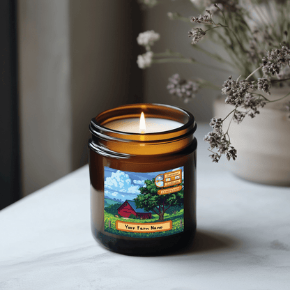 A lit Stardew Valley scented candle is displayed in an amber jar featuring a custom farm design and seasonal information.
