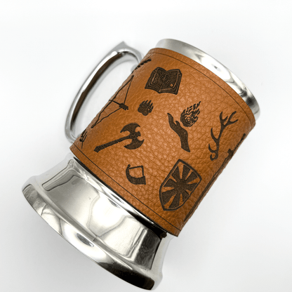 A steel beer mug is wrapped in upcycled leather featuring etched designs reminiscent of a DnD adventurer's starter kit.