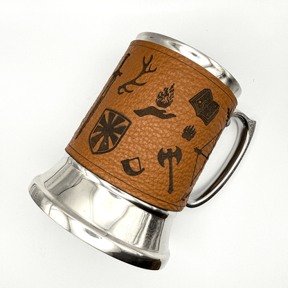 A steel beer mug is wrapped in upcycled leather featuring Dungeons and Dragons-inspired designs like antlers, a shield, and an axe.