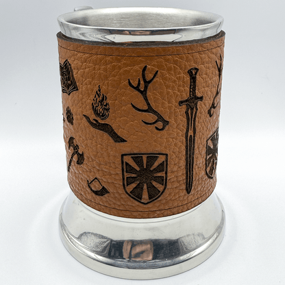 A steel beer mug is wrapped in upcycled brown leather featuring a Dungeons and Dragons adventurer's starter kit design of symbols including a sword, shield, flame, and stag.