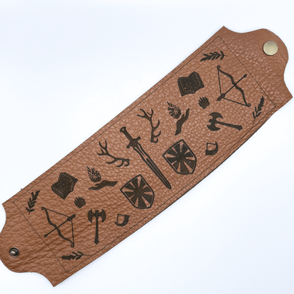 A brown upcycled leather wrap features laser-etched Dungeons and Dragons imagery including a sword, shield, bow, and other fantasy symbols.