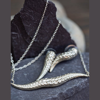 Silver necklace with intricate tentacle design on a dark stone surface