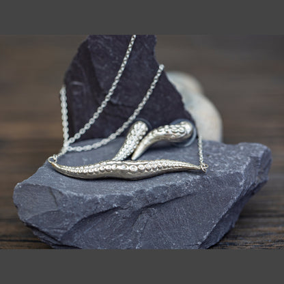 Silver necklace with a tentacle-shaped pendant on a dark stone surface