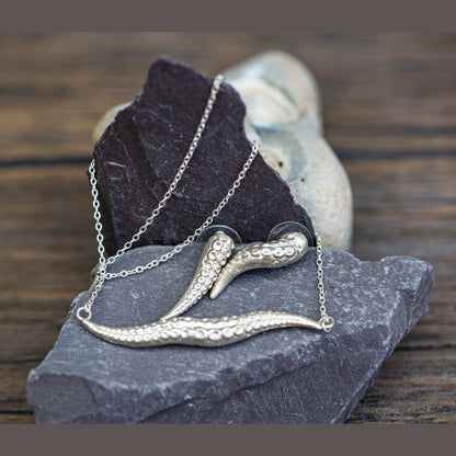 Silver necklace with tentacle-like design on a dark stone surface