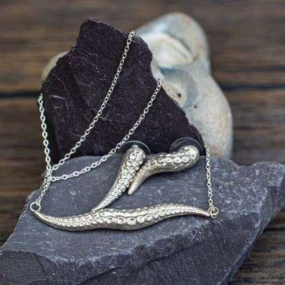 Silver octopus necklace on a dark stone surface with a wooden background