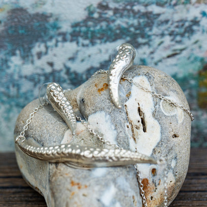 Silver tentacle-shaped pendant on a textured stone surface with a blurred natural background
