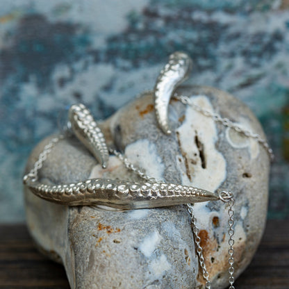 Silver octopus tentacle-shaped necklace on a textured stone surface with a blurred natural background
