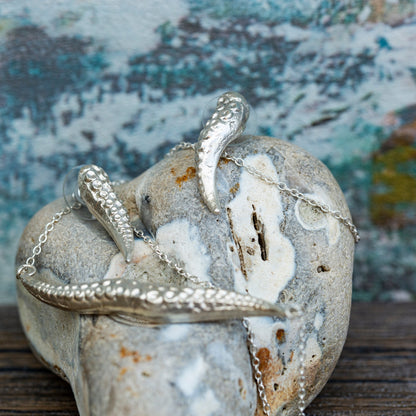 Silver jewelry piece on a textured stone surface with a blurred natural background