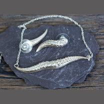 Silver necklace with kraken tentacle design on a dark stone surface