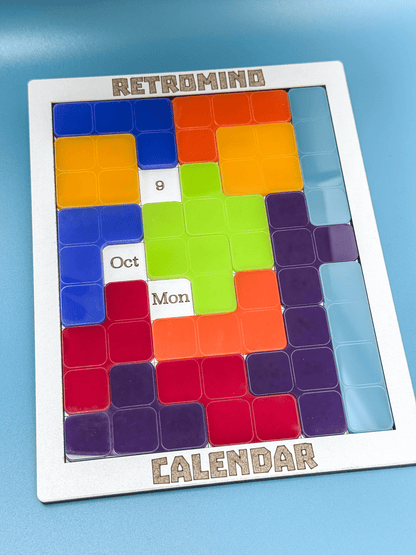 The RetroMind KronoBlox puzzle calendar displays the date as October 9th, Monday, using colorful Tetromino-shaped blocks arranged within a silver frame.