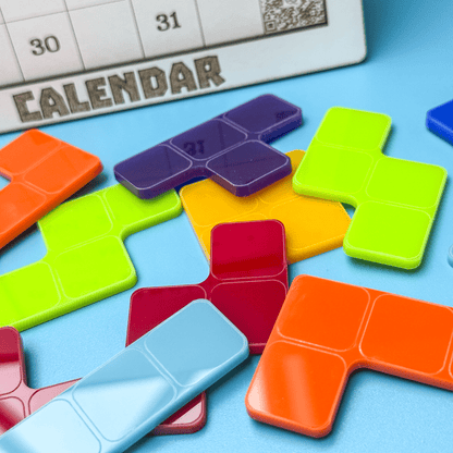 Colorful KronoBlox puzzle pieces arranged on a blue surface next to a calendar page displaying the number thirty-one.