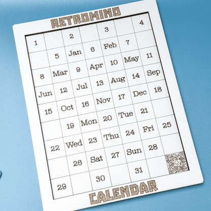 A white KronoBlox puzzle calendar displays dates and days of the week arranged in a Tetromino shape on a blue surface.