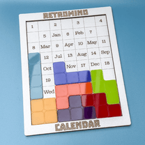 A KronoBlox puzzle calendar displays dates arranged as Tetromino blocks on a white board against a blue background.