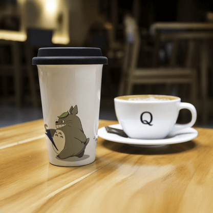 Ceramic travel mug with Totoro from Studio Ghibli and a Quirkify coffee cup on a wooden table.