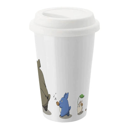 A white insulated ceramic travel mug features Studio Ghibli's Totoro and other characters from the anime in a whimsical illustration.