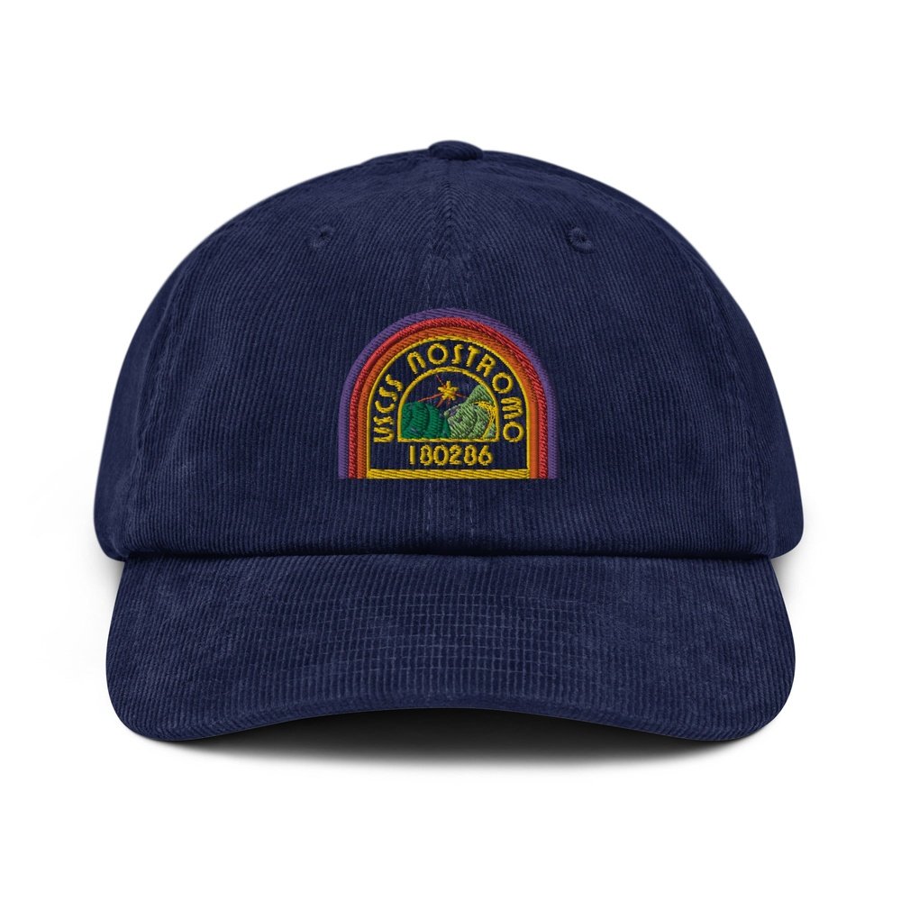 A navy blue corduroy baseball cap features an embroidered logo of the USCSS Nostromo with a rainbow arc and the number 180286.