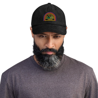 A person wears a black Alien USCSS Nostromo embroidered dad hat featuring a rainbow-style logo on the front.