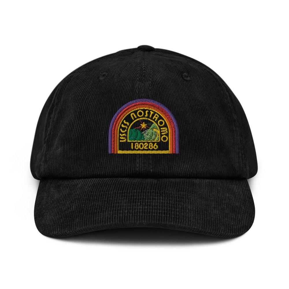 A black corduroy baseball cap features an embroidered logo of the USCSS Nostromo spaceship with a rainbow-colored design and the number 180286.